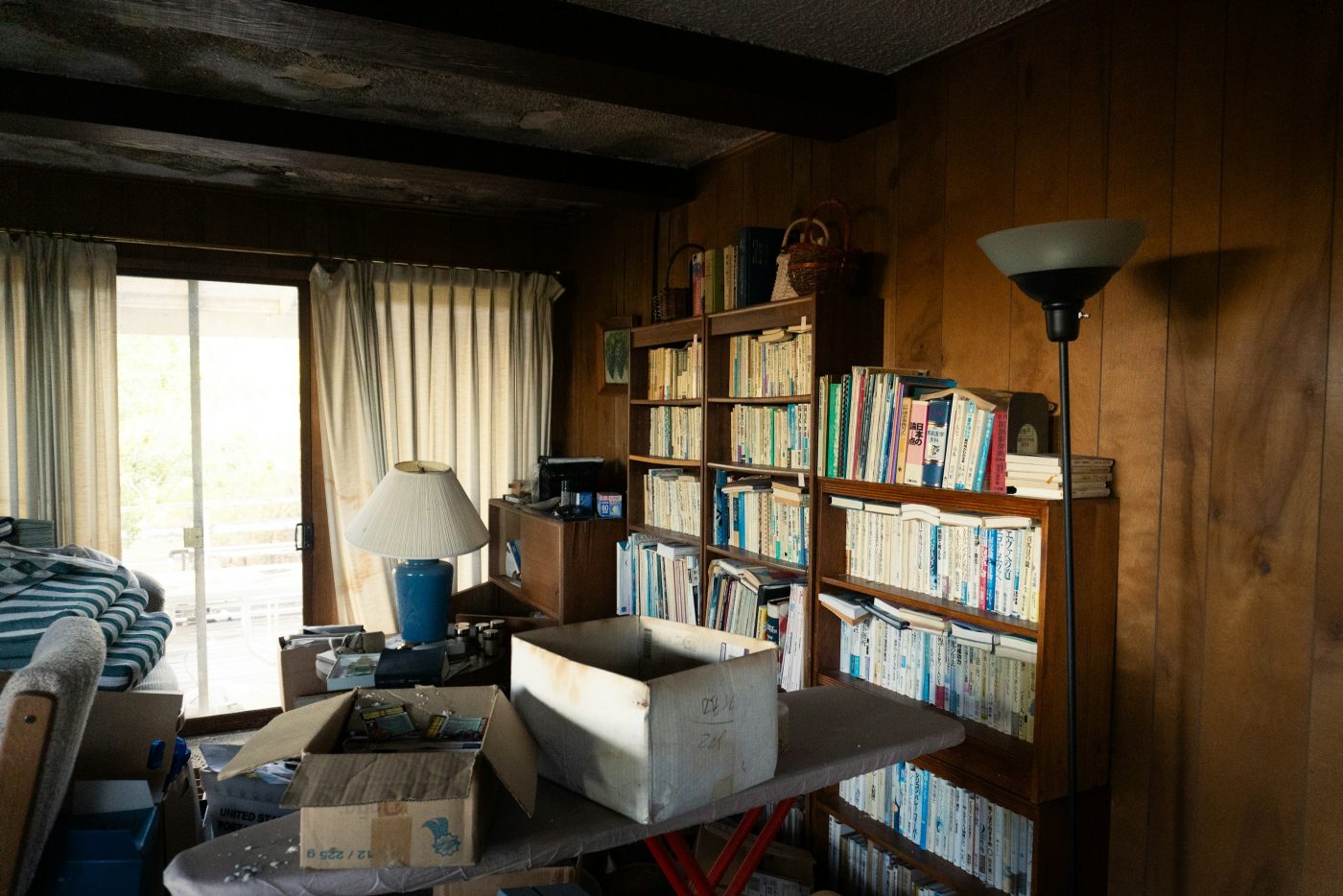 La habitación de una casa llena de cajas de cartón, libros y muebles amontonados sobre una tabla de planchar. Foto: Naveen Ketterer en Unsplash.