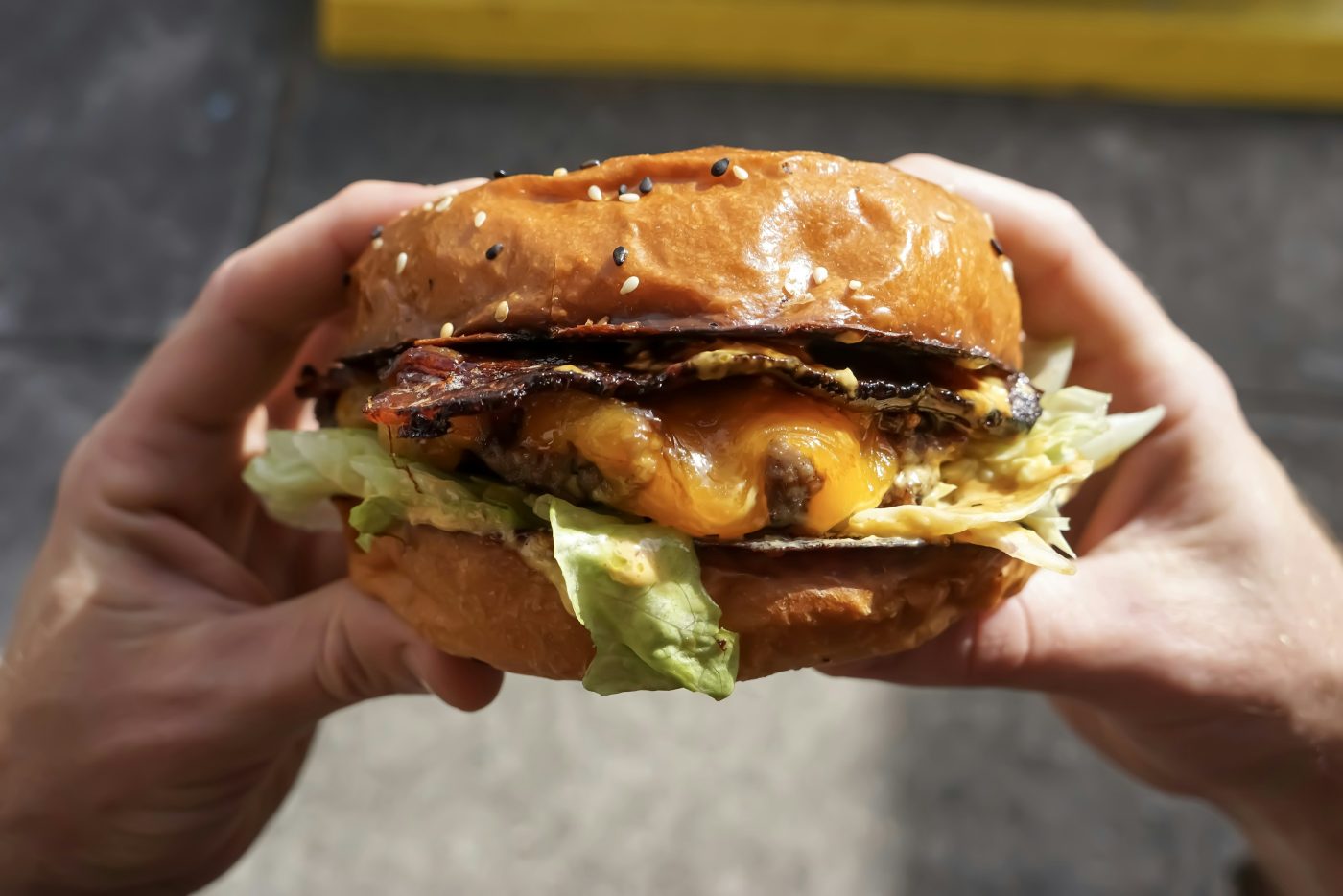 Una hamburguesa con queso, beicon y lechuga, lista para comer con las manos.