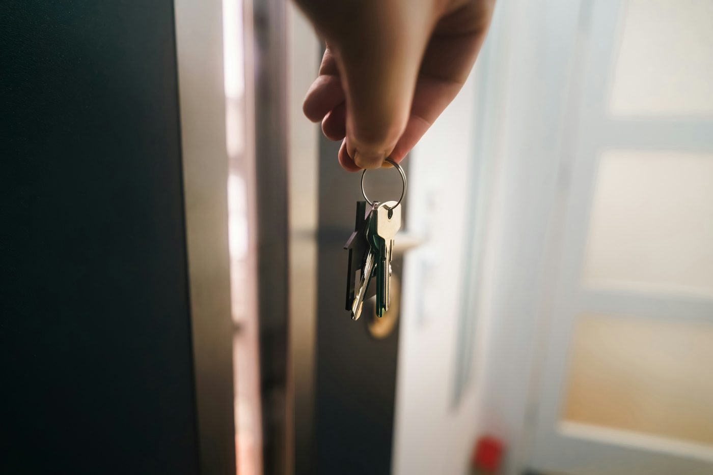 Una mano sostiene las llaves de casa junto a la puerta entreabierta.