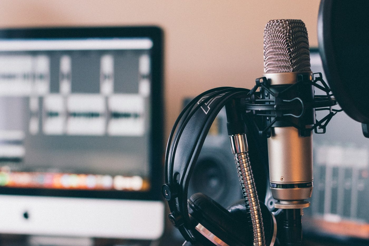 Un micrófono de estudio con unos auriculares colgados y, al fondo, una pantalla con un programa de edición de sonido. Foto: Will Francis en Unsplash.